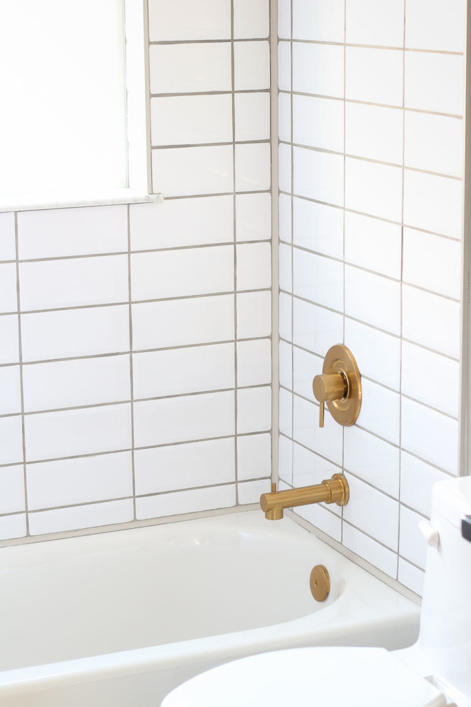 modern stacked white subway tile with gold tub spout and handle