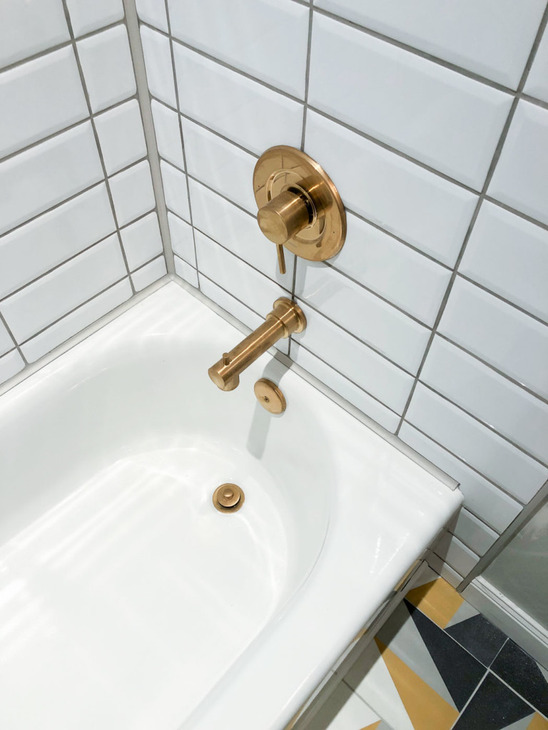 brushed gold moen tub spout and mixing valve in white tub and white tiles
